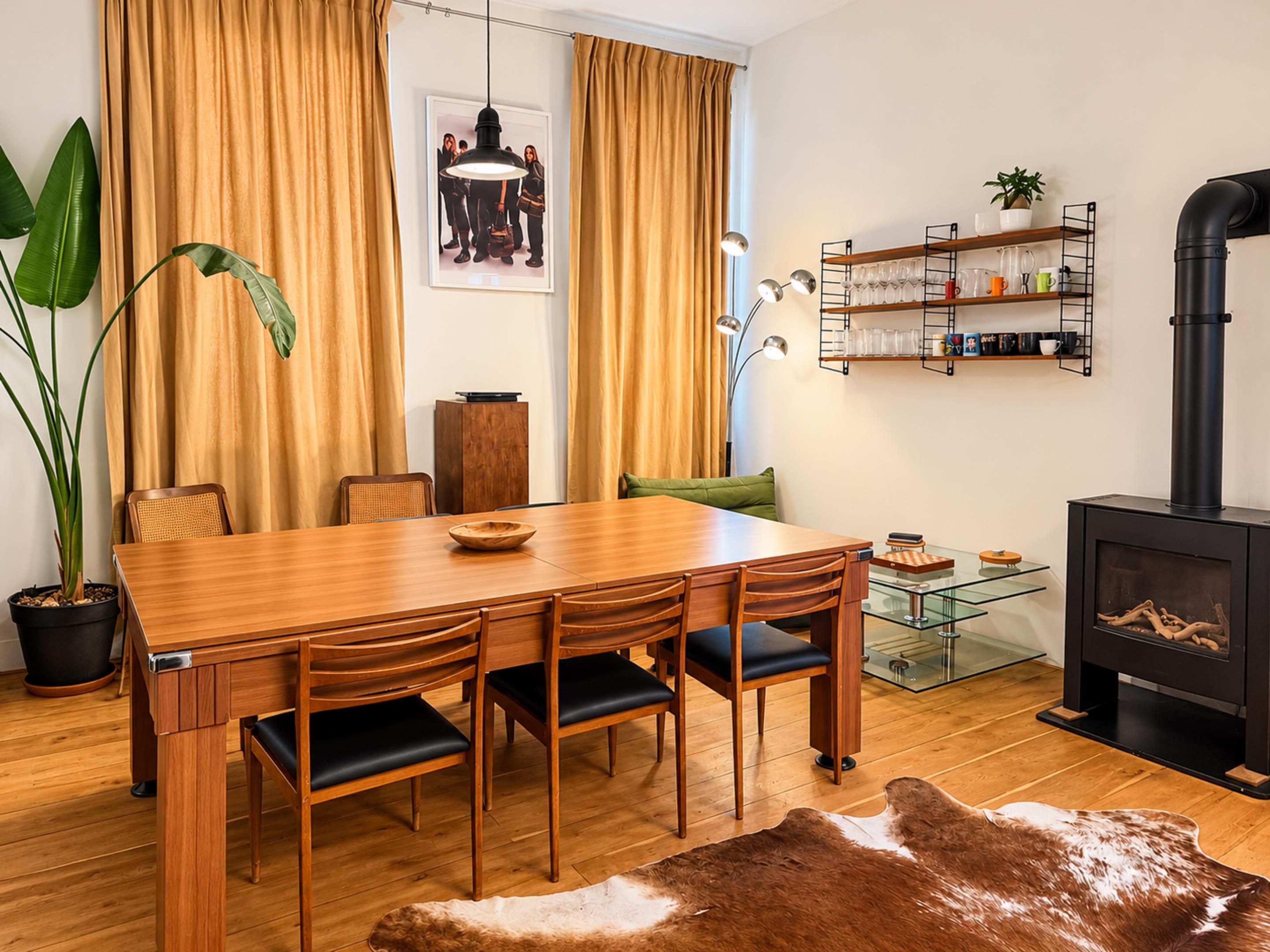 Un salon moderne avec une table à manger en bois, des chaises, une table basse en verre, une cheminée noire et une plante en pot.