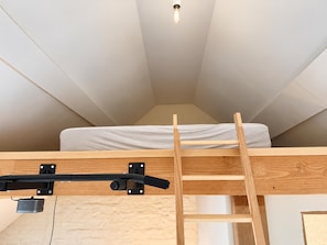 A loft bedroom with a wooden ladder leading to a bunk bed, a ceiling light, and a window.