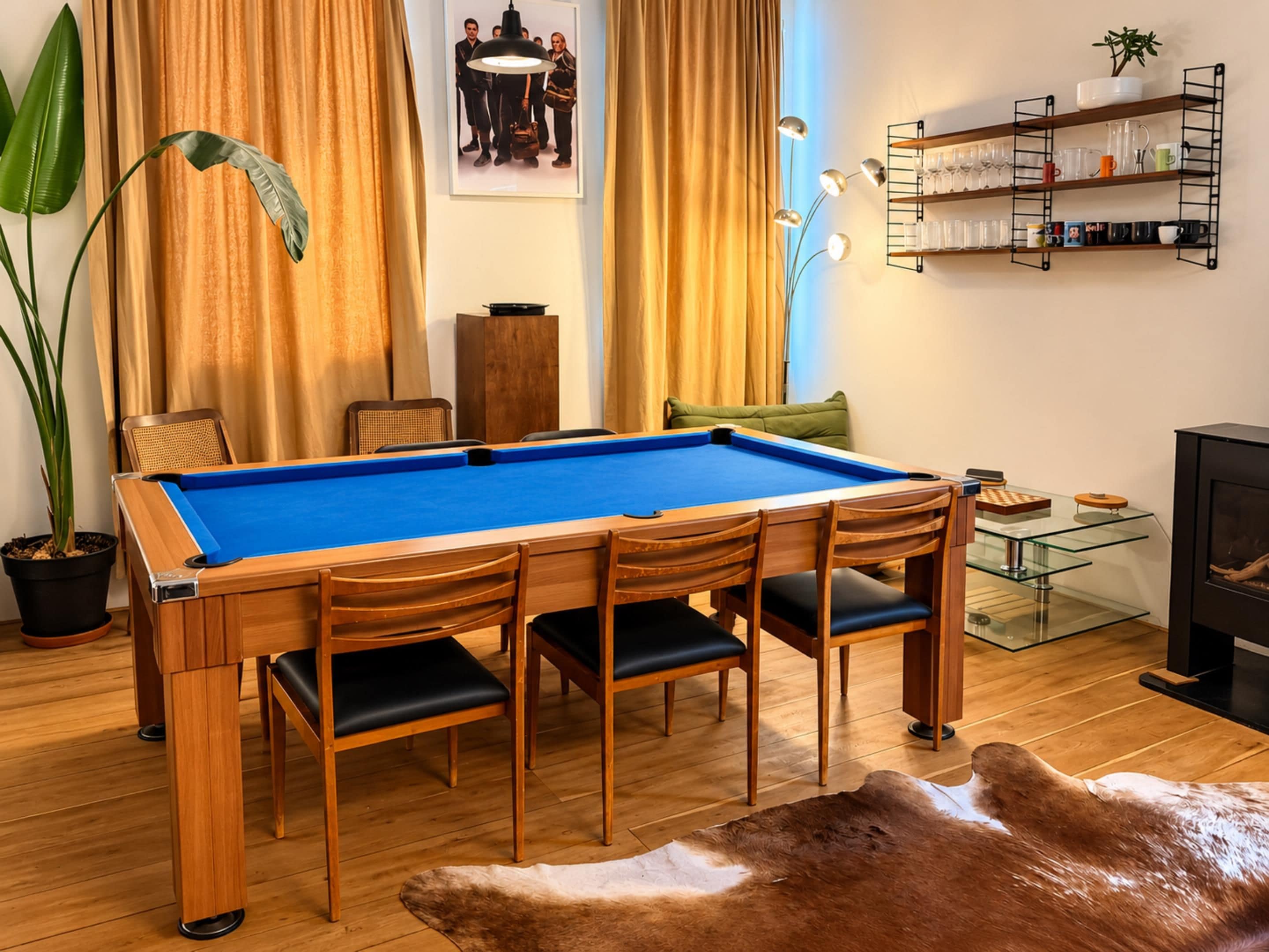 Een pooltafel met stoelen, een glazen bijzettafeltje, een bank, een open haard en een plank met glazen.