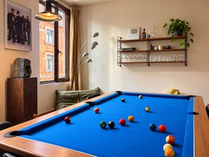 A pool table with balls, a framed picture, a shelf with glasses, and a plant.