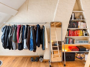 Una habitación con un perchero, una escalera y una estantería con libros y un radio.