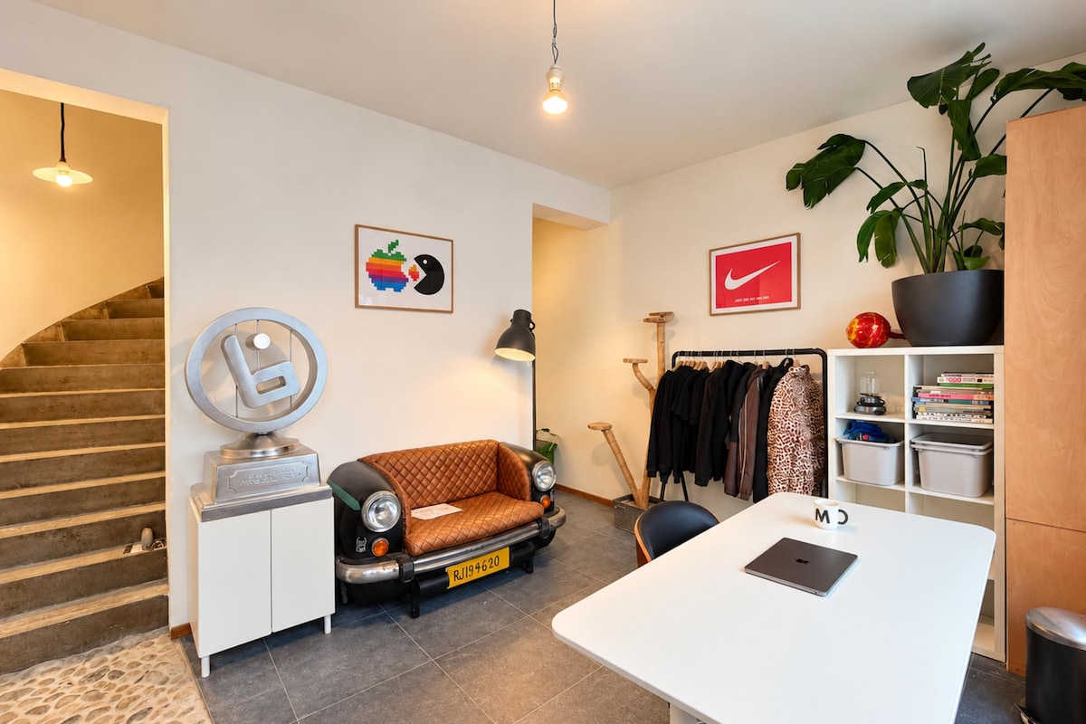 A modern living space with a sofa, a desk, a coat rack, and a staircase.