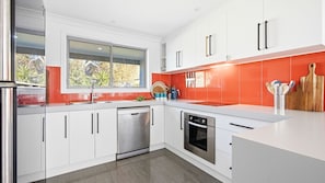 Eine moderne Küche mit weißen Schränken, Edelstahlgeräten und einer roten Spritzschutzwand.