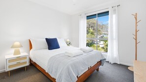 Ein Hotelzimmer mit Bett, Nachttisch, Lampe und Blick ins Freie durch ein Fenster.