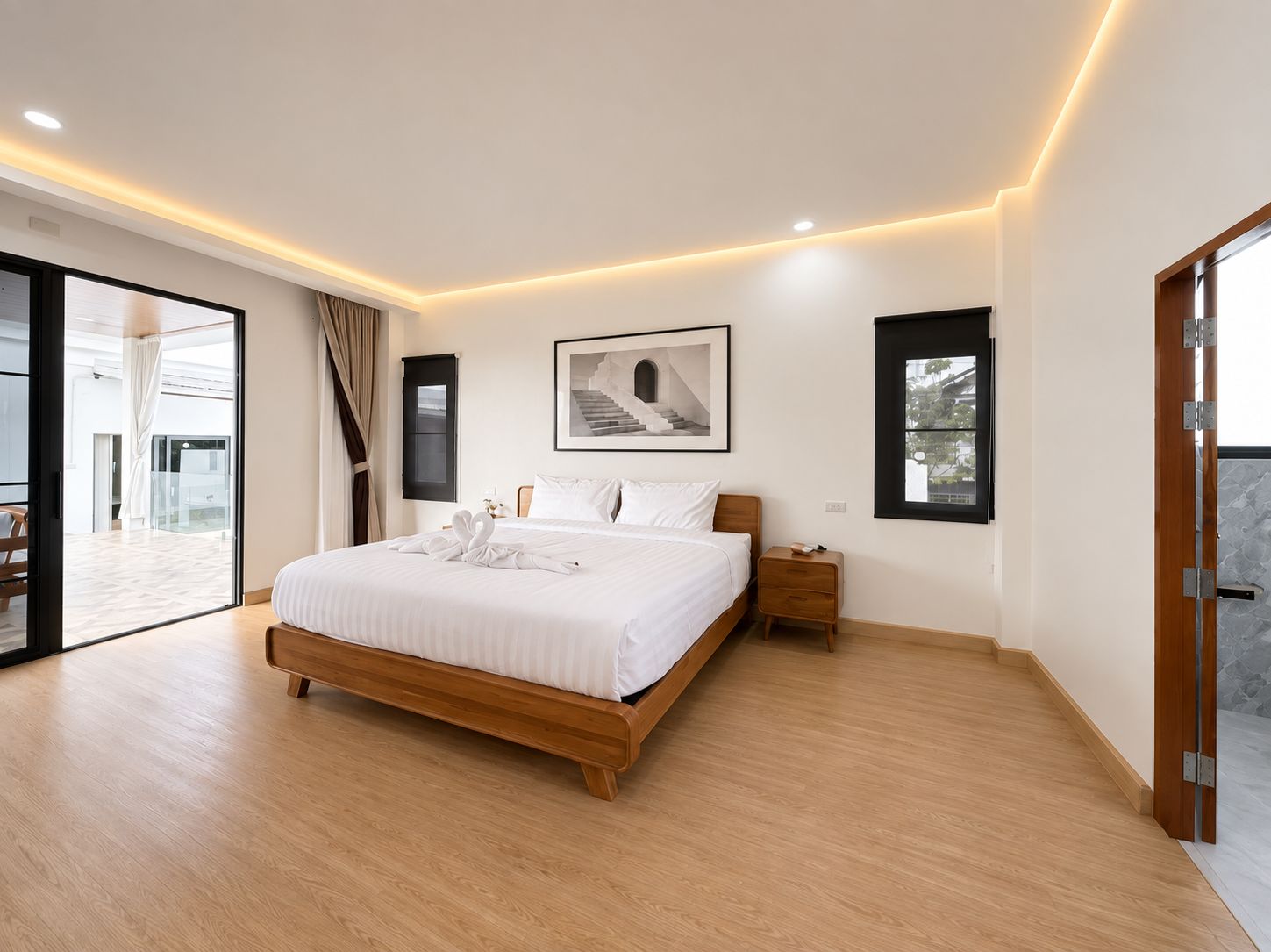 A modern bedroom with a large bed, a nightstand, a framed picture, and a sliding glass door leading to an outdoor area.