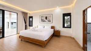 Une chambre moderne avec un grand lit, une table de chevet, un tableau encadré et une porte-fenêtre coulissante donnant sur un espace extérieur.