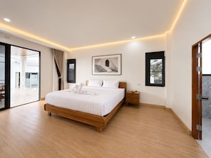 A modern bedroom with a large bed, a nightstand, a framed picture, and a sliding glass door leading to an outdoor area. - Yun Prestige Villa: 6 Bedrooms, Private Pool & Garden (Tambon Nong Phueng)