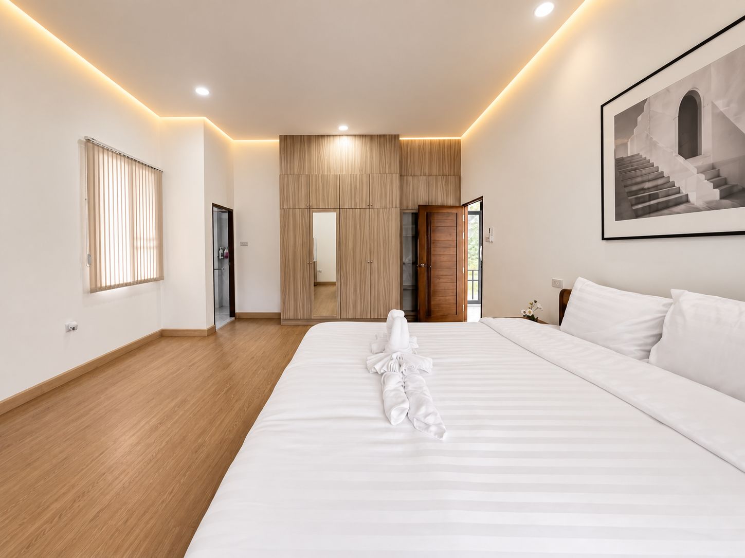 Habitación de hotel con una cama grande, suelo de madera, un armario, un espejo y un cuadro en la pared.