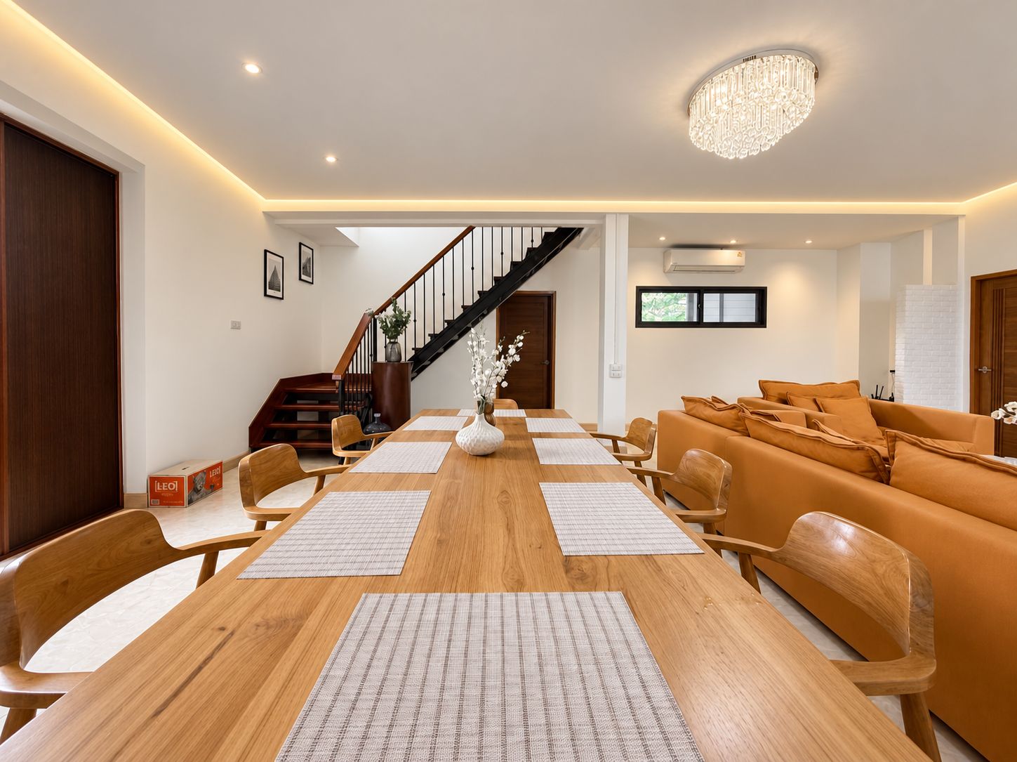 En moderne stue med et træspisebord, orange sofa og en trappe, der fører op til en etage.