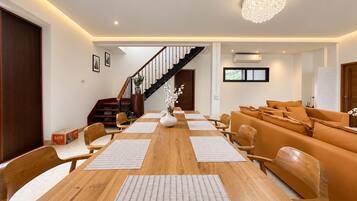 A modern living room with a wooden dining table, orange sofa, and a staircase leading to an upper level.