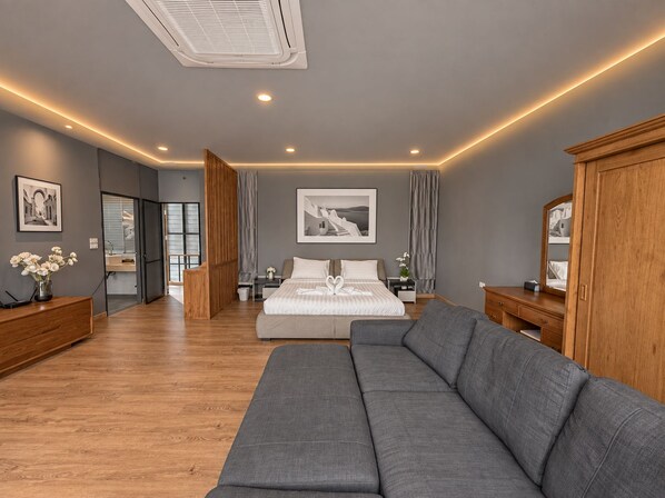 A modern bedroom with a large bed, a grey sofa, wooden furniture, and artwork on the walls.