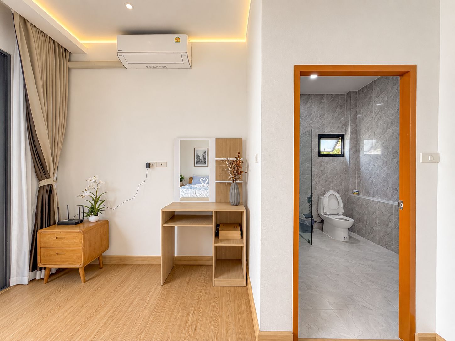 A modern room with a desk, a small cabinet, a potted plant, and a bathroom with a toilet and shower.