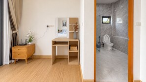 Une chambre moderne équipée d’un bureau, d’un petit meuble de rangement, d’une plante en pot et d’une salle de bain avec des toilettes et une douche.