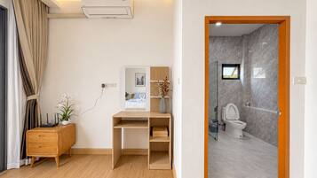 A modern room with a desk, a small cabinet, a potted plant, and a bathroom with a toilet and shower.