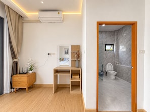 A modern room with a desk, a small cabinet, a potted plant, and a bathroom with a toilet and shower. - Yun Prestige Villa: 6 Bedrooms, Private Pool & Garden (Tambon Nong Phueng)