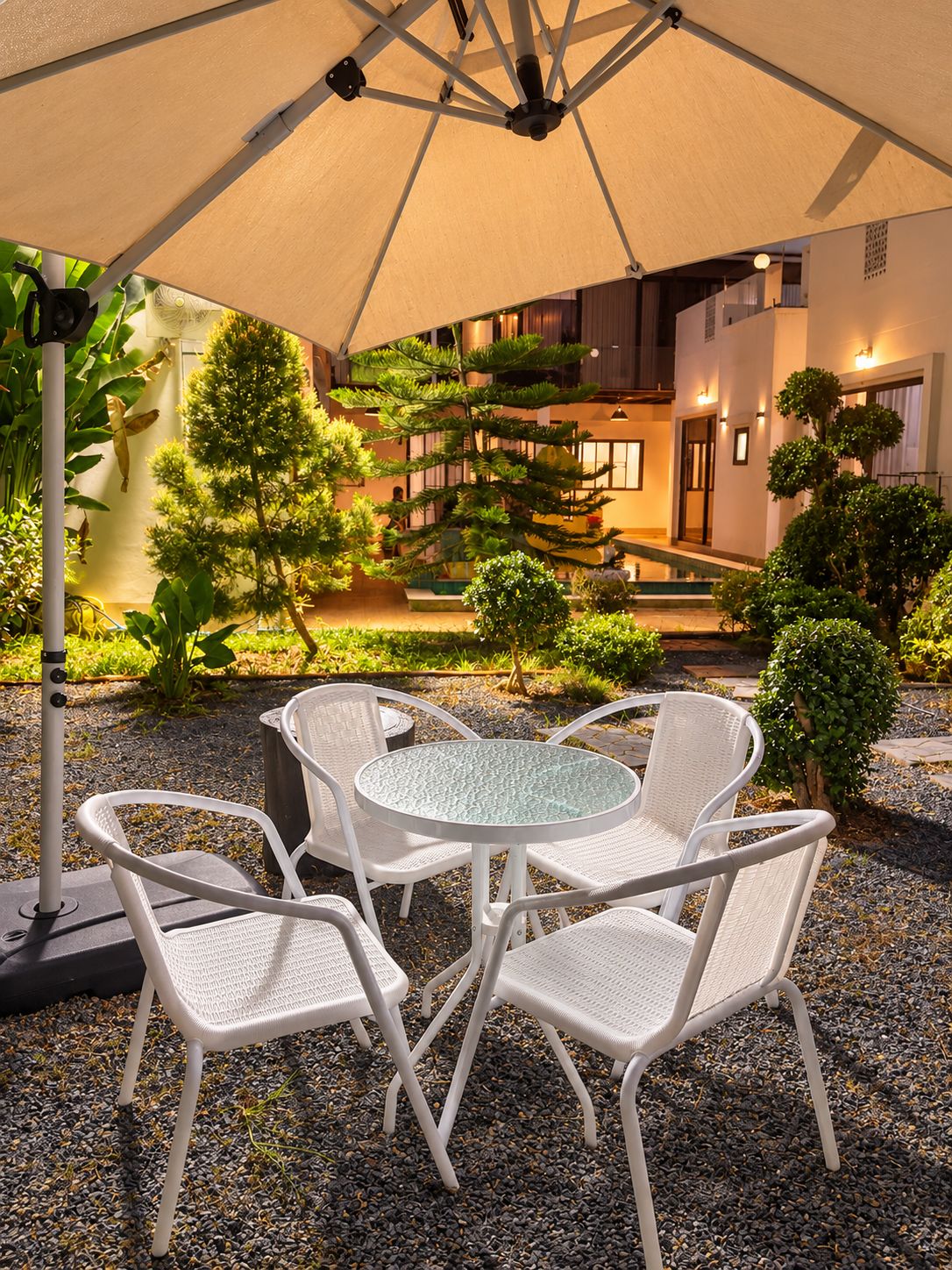 An outdoor seating area with a round table and four chairs, surrounded by gravel and plants.