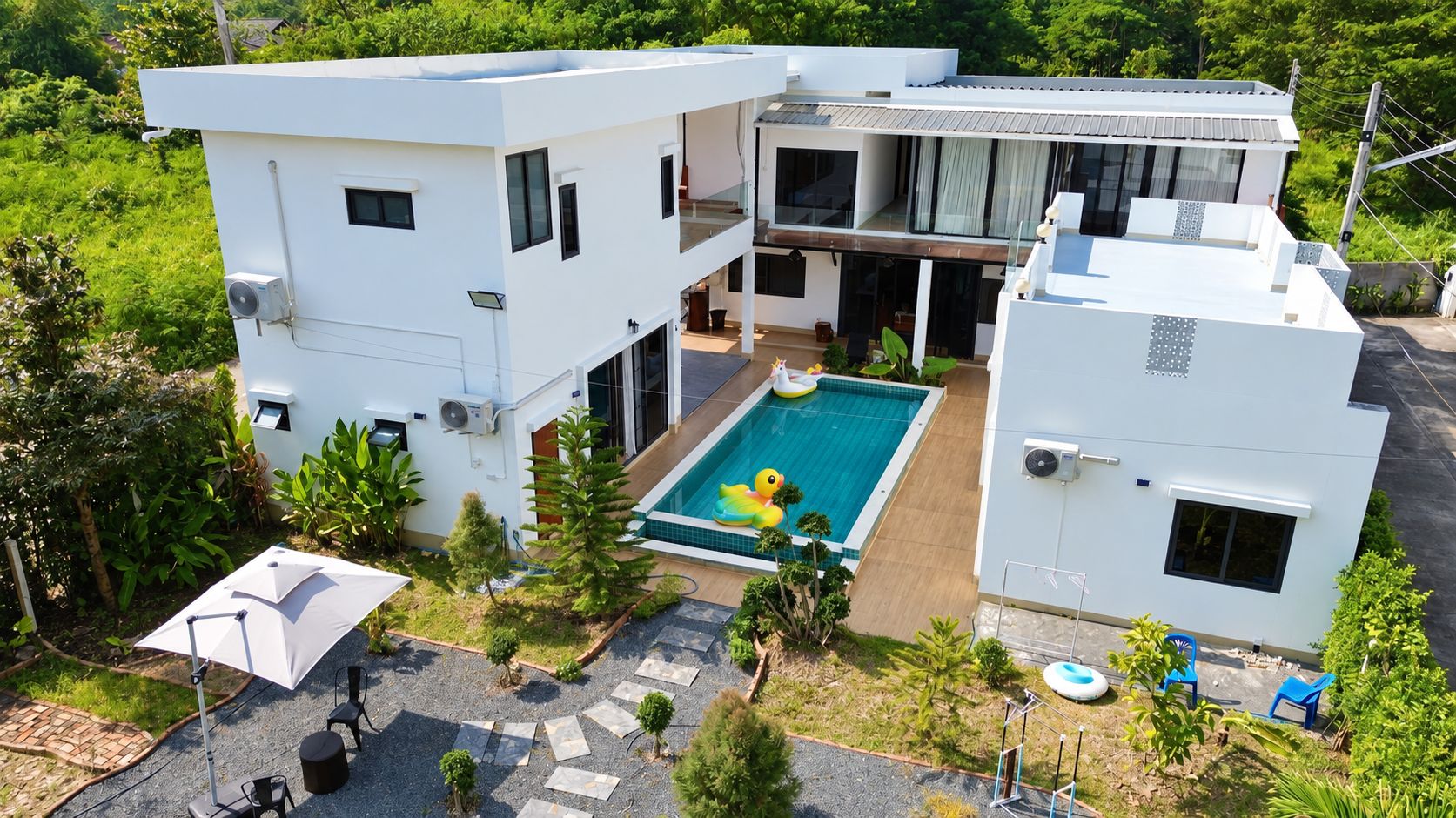 A modern two-story house with a swimming pool, surrounded by greenery and a paved patio area.