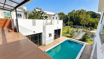 Un edificio moderno con piscina en la azotea, barandillas de vidrio y vistas a una zona residencial.