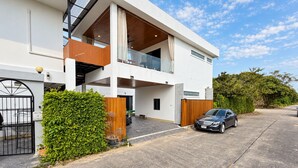 Une maison moderne à deux étages, dotée d’un garage, d’un balcon et d’une voiture garée devant.