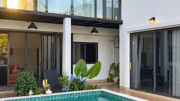 Ett modernt hus med en swimmingpool, stora fönster och en balkong.