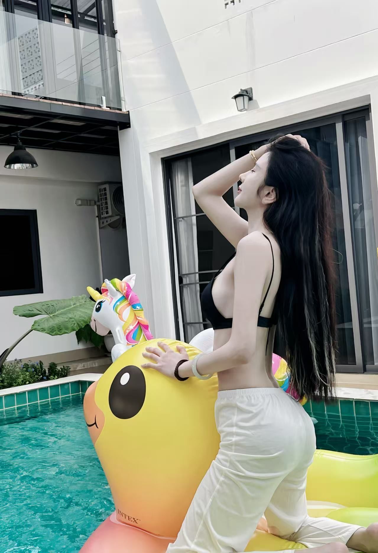 A person sitting on a yellow inflatable unicorn toy by a swimming pool.