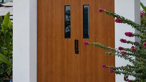 Um portão de madeira com design moderno, em frente a uma parede branca com uma pequena janela.