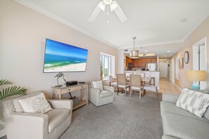 Een woonkamer met een flatscreen televisie, een bureau en een eethoek met stoelen en een tafel.