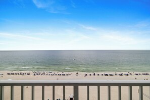 Een strand met parasols en mensen, bekeken vanuit een balkon.