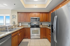 A kitchen with wooden cabinets, stainless steel appliances, granite countertops, and a view to the outside. - Seawind 1109 by Liquid Life (Gulf Shores)