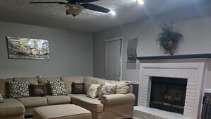 A living room with a sectional sofa, a fireplace, and a ceiling fan. - Charming 3-bedroom house in Rex near Atlanta (Rex)
