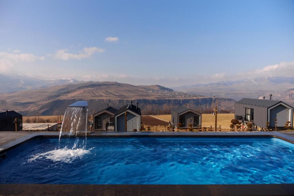 A swimming pool with a waterfall feature, surrounded by modern buildings with a mountainous backdrop.