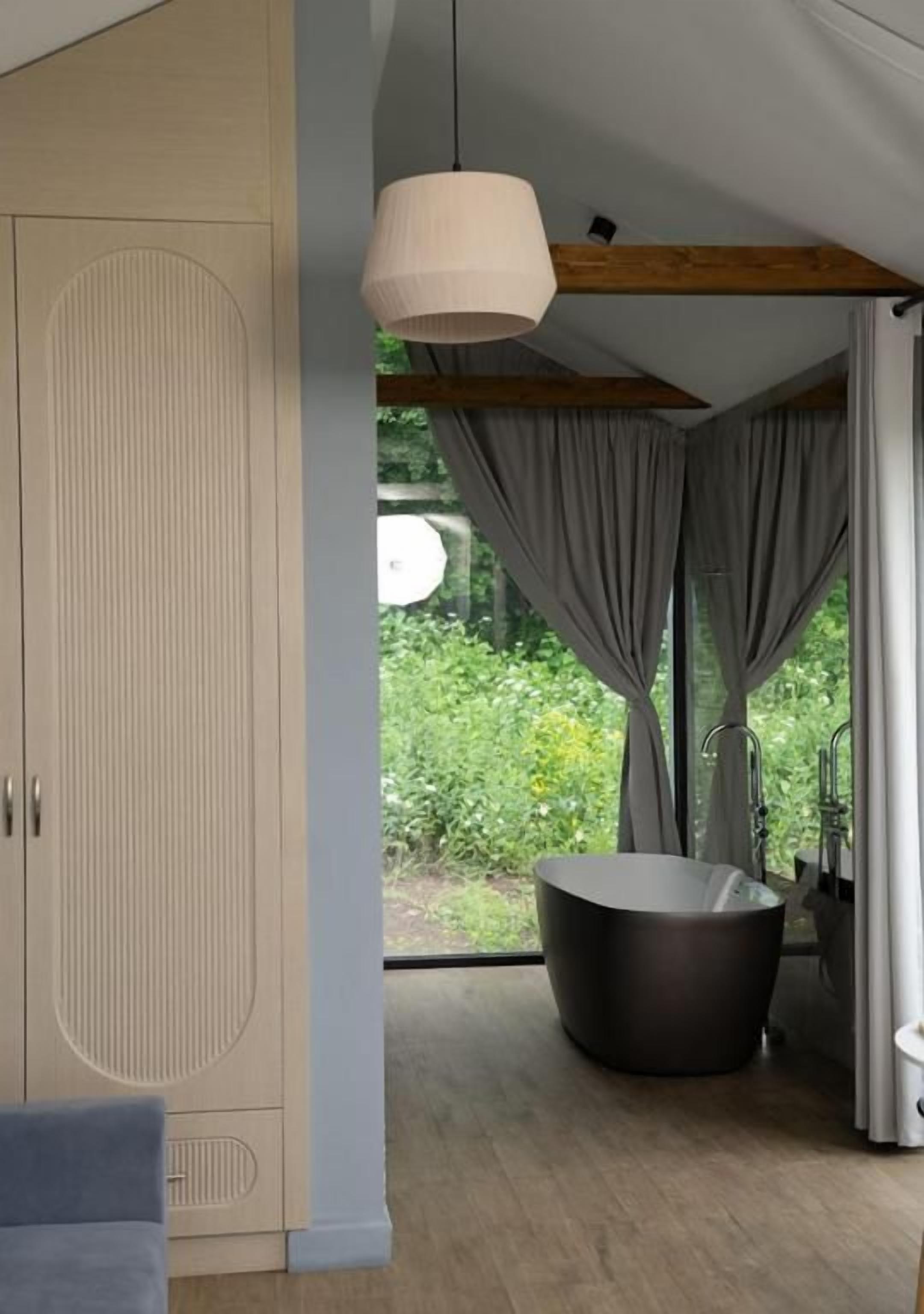 A modern bathroom with a bathtub, a wooden ceiling beam, and a large window with curtains.