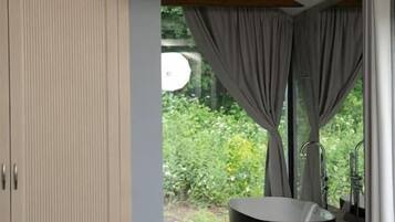 A modern bathroom with a bathtub, a wooden ceiling beam, and a large window with curtains.