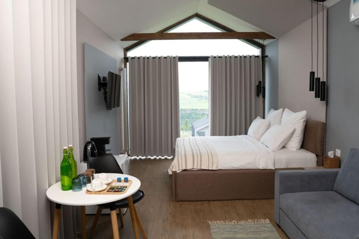 A bedroom with a bed, a sofa, a table with breakfast items, and a view through the window.