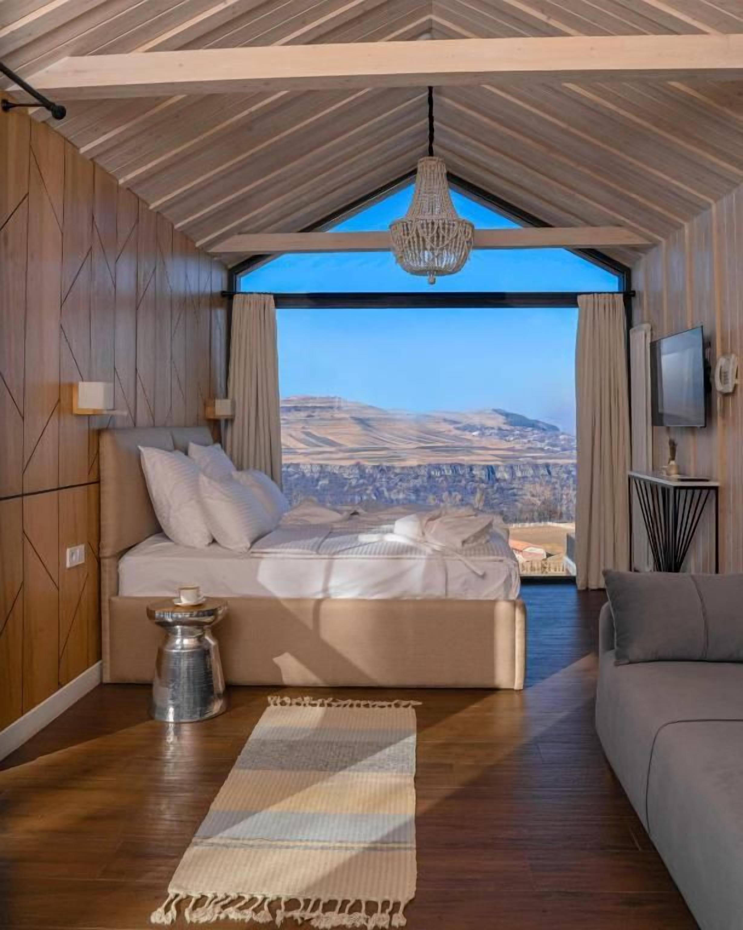 A bedroom with a large bed, a view of the landscape, a chandelier, and a television.
