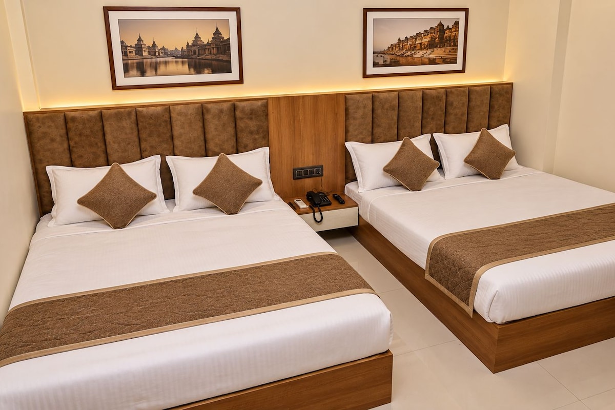 A hotel room with two beds, a wooden headboard, a bedside table with a phone, and framed pictures on the wall.