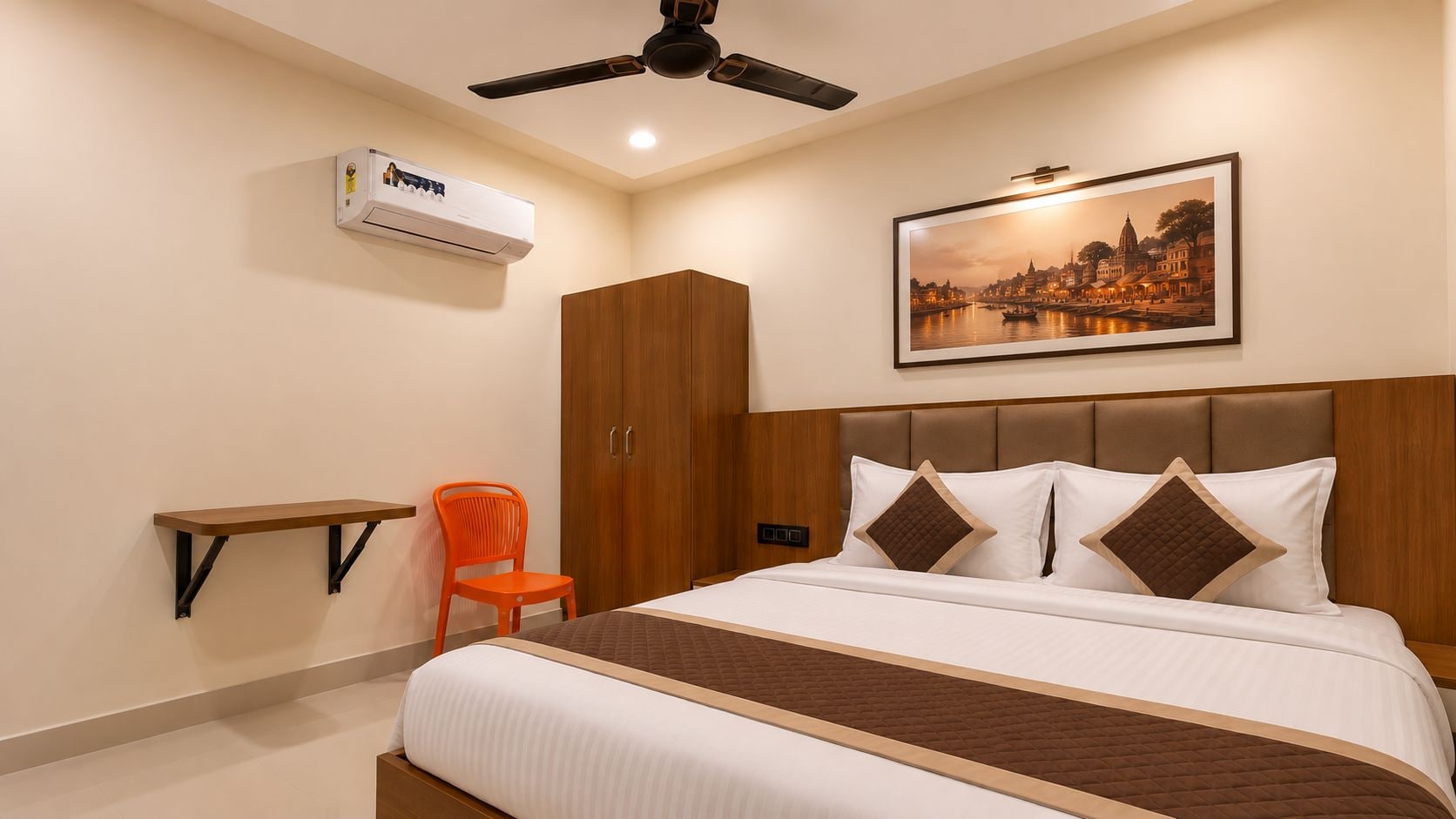 A hotel room with a bed, a chair, a wardrobe, an air conditioning unit, and a framed picture on the wall.