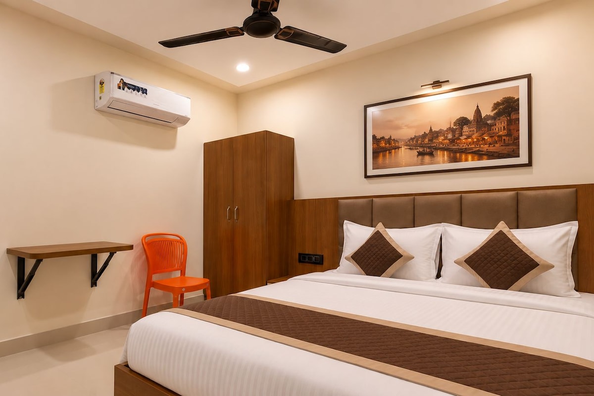 A hotel room with a bed, a chair, a wardrobe, an air conditioning unit, and a framed picture on the wall.