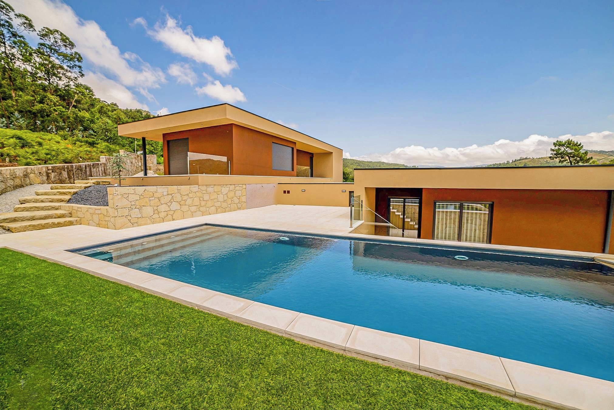 Una casa moderna con piscina, scalini in pietra e prato.