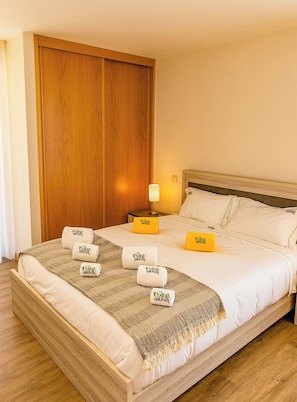 A hotel room with a wooden bed, a nightstand with a lamp, and multiple towels with a logo. - Nature Hill 1 by Portugal Active (Viana do Castelo)
