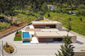 Ein modernes, zweistöckiges Gebäude mit Swimmingpool, umgeben von Grünflächen und Hügeln.