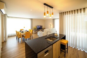 A modern kitchen with a central island, dining area with yellow chairs, and a living room with a sofa and TV. - Nature Hill 1 by Portugal Active (Viana do Castelo)