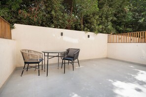 An outdoor patio with a table and two chairs, surrounded by a low wall and dense foliage. - Lovely Home at Elevens by Spacey #1 (cairo)