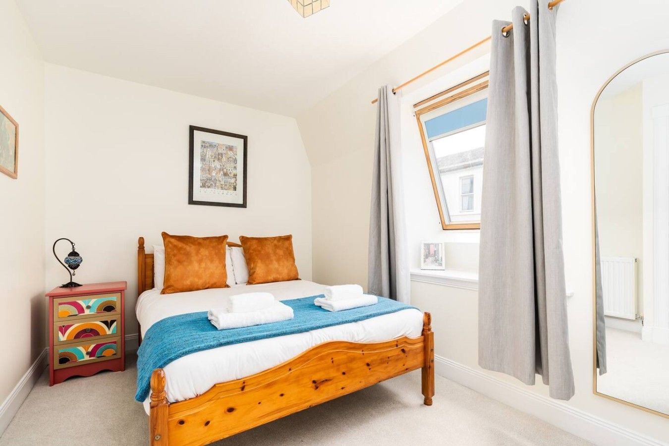 A bedroom with a wooden bed, a nightstand, a window with curtains, and a framed picture on the wall.