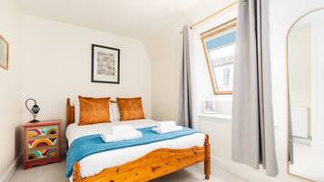 A bedroom with a wooden bed, a nightstand, a window with curtains, and a framed picture on the wall.
