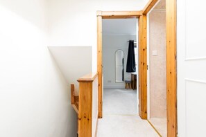 A narrow hallway with wooden walls and a carpeted floor leading to a room with a mirror and a chair. - Potter`s House | Central 2 Bed, Sleeps 4 (Edinburgh)