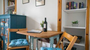 A room with a wooden table, two chairs, a cabinet, and shelves with books and a plant.