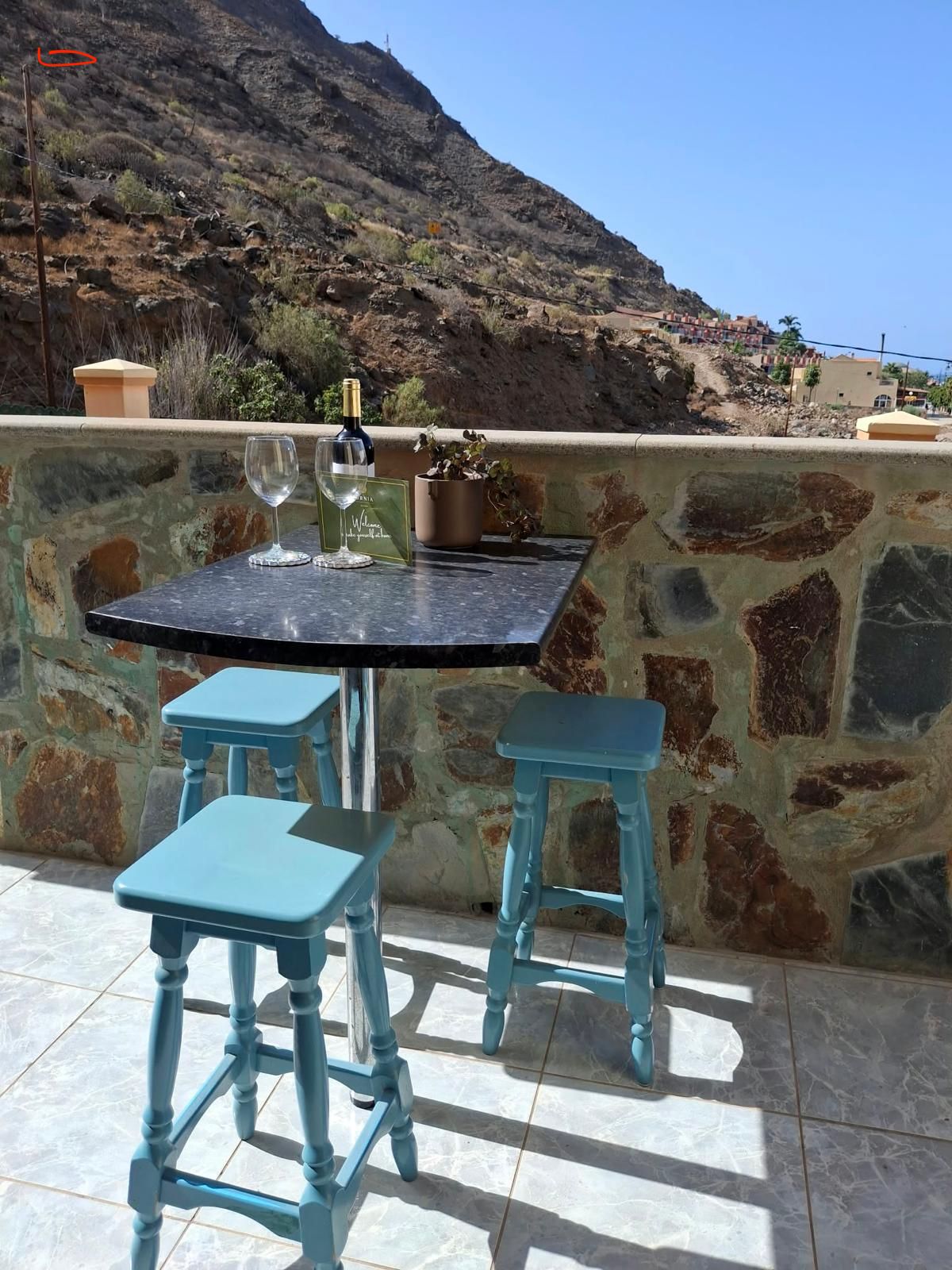 An outdoor patio with a table and two stools, a wine bottle, and a glass.