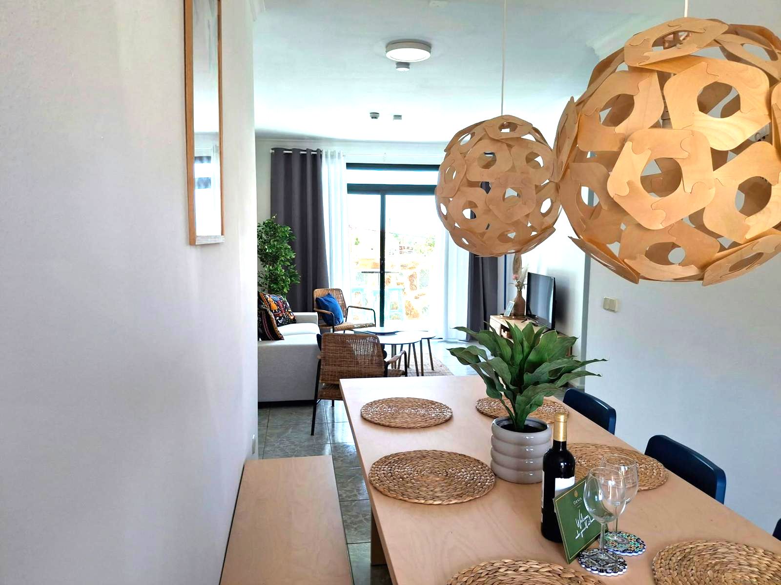 Un espace repas moderne avec une longue table en bois, des sets de table en fibres tressées et une plante en pot.