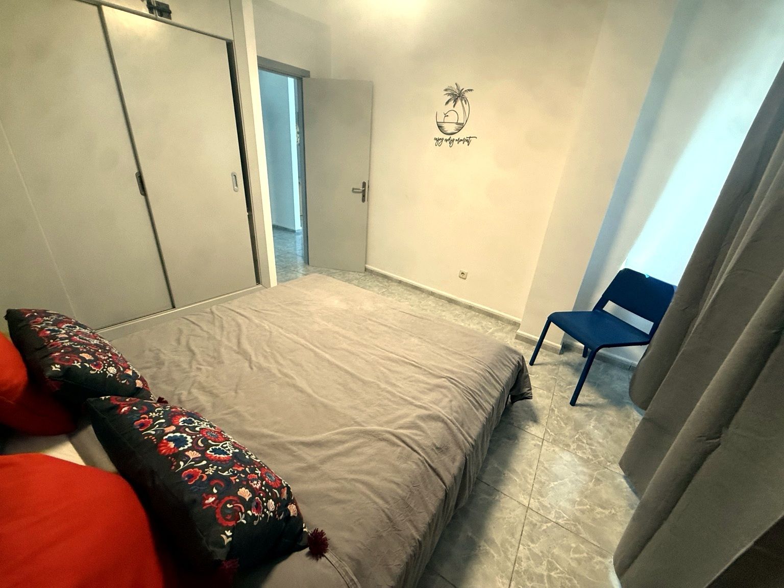 Ein Schlafzimmer mit einem Bett, einem Sessel, einer Tür und einer Wand mit einem Logo.